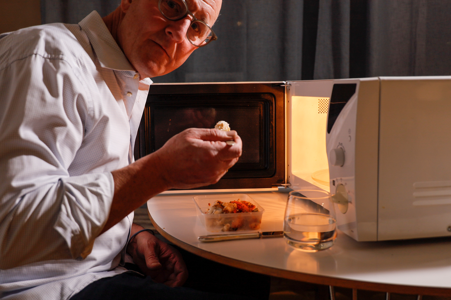 Äldre man som äter mikrovågsvärmd mat framför en mikrougn