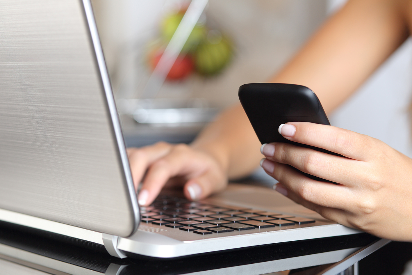 En kvinnlig hand håller i en telefon bredvid en laptop