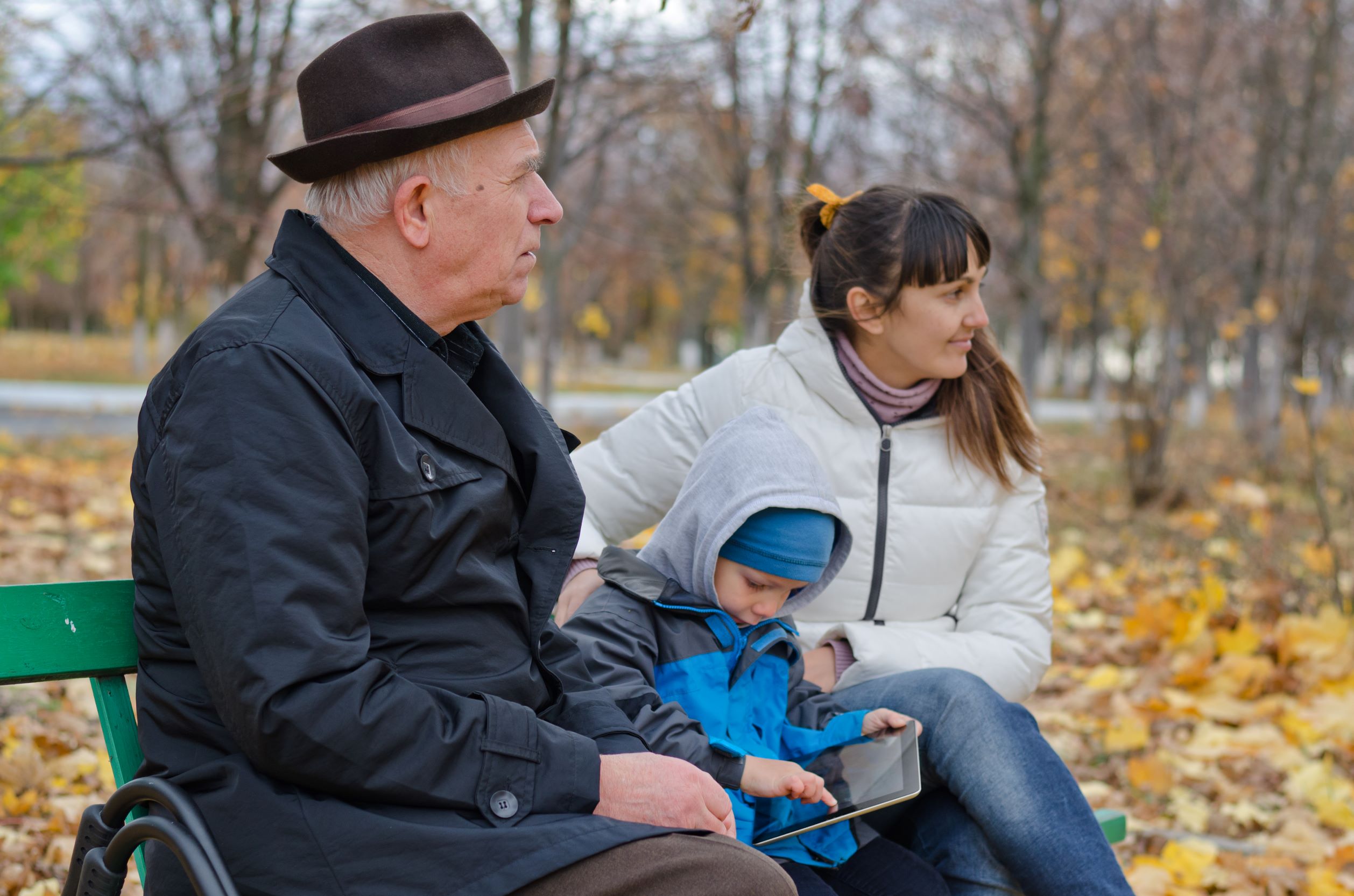 Äldre man, ung kvinna och barn sitter på en parkbänk tillsammans