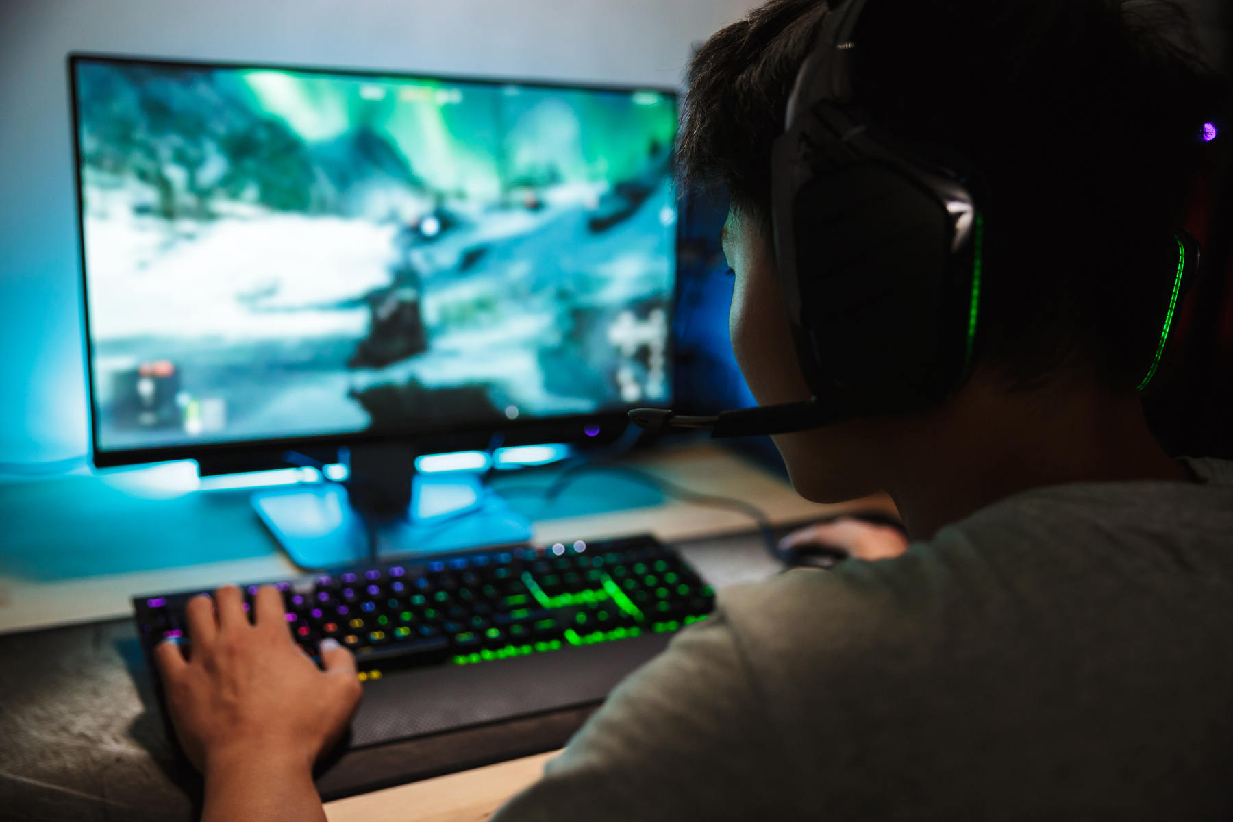En tonårspojke sitter och spelar dataspel vid en stor skärm.