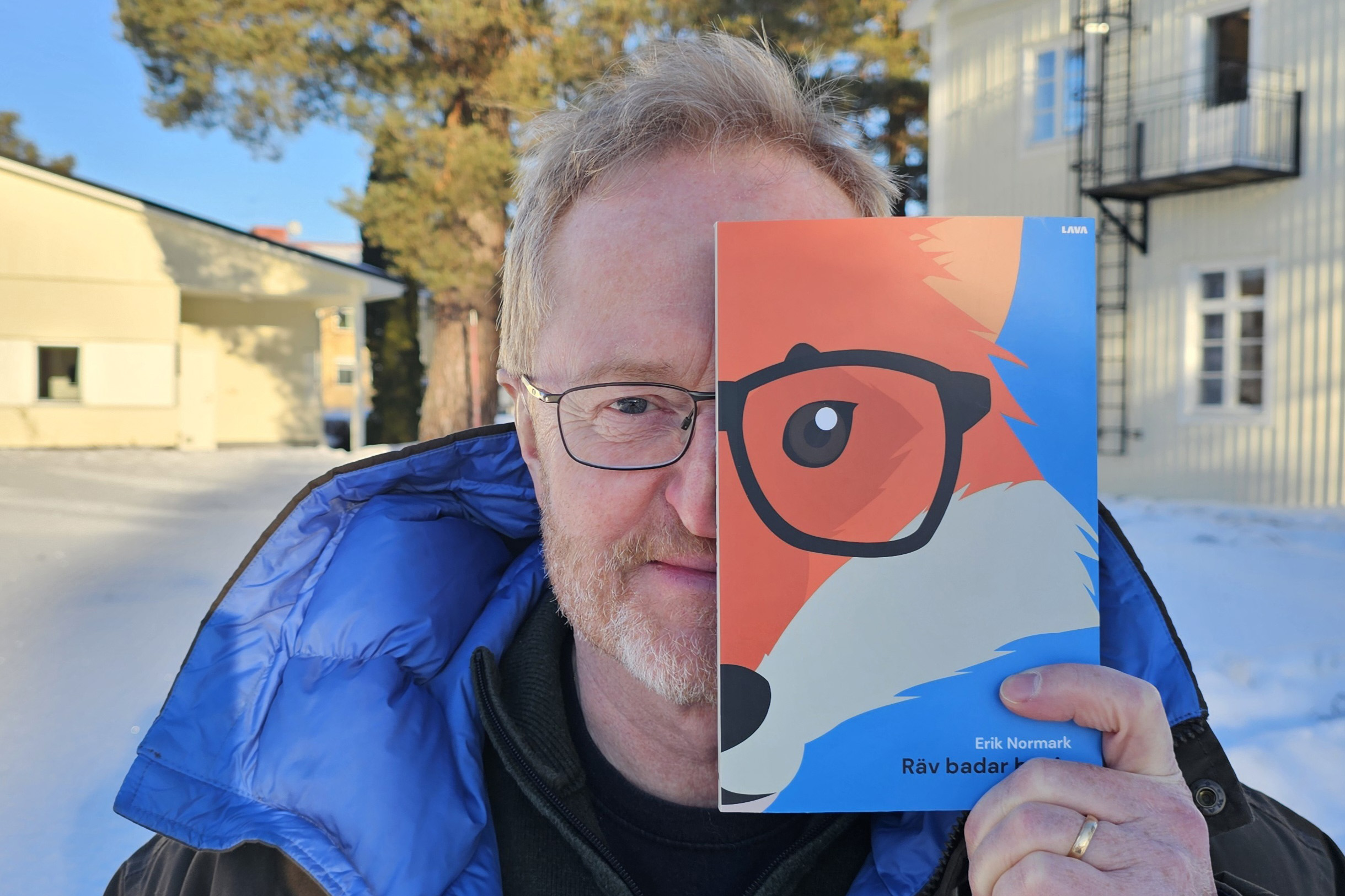 En man står utomhus och håller upp en bok med en räv på framför halva ansiktet.