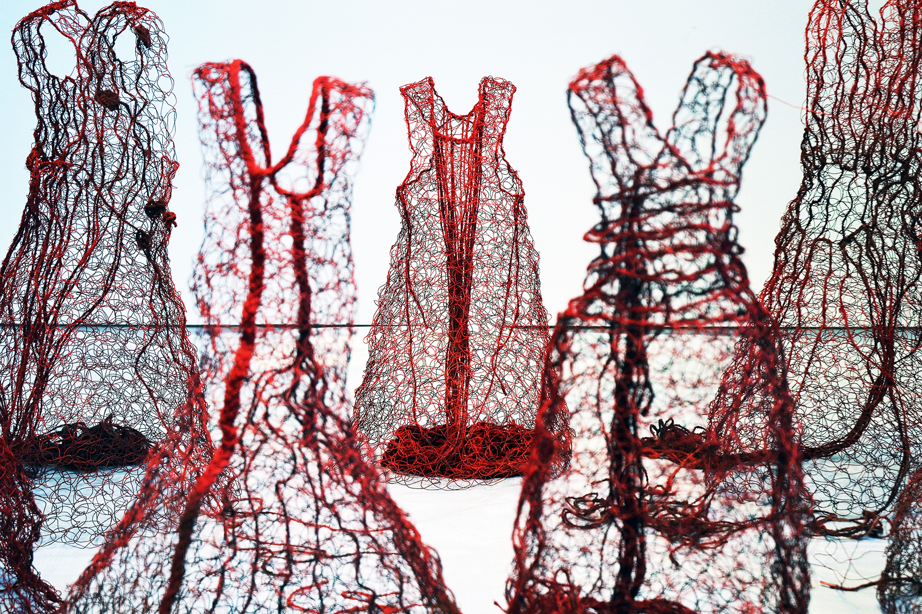 Skulpturer formade som klänningar gjorda i rödfärgade grova nät